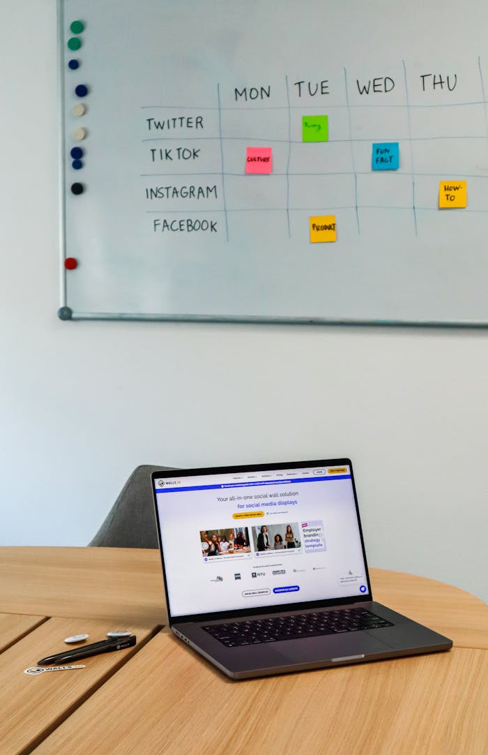 A modern office setup featuring a laptop and a whiteboard schedule for social media platforms.